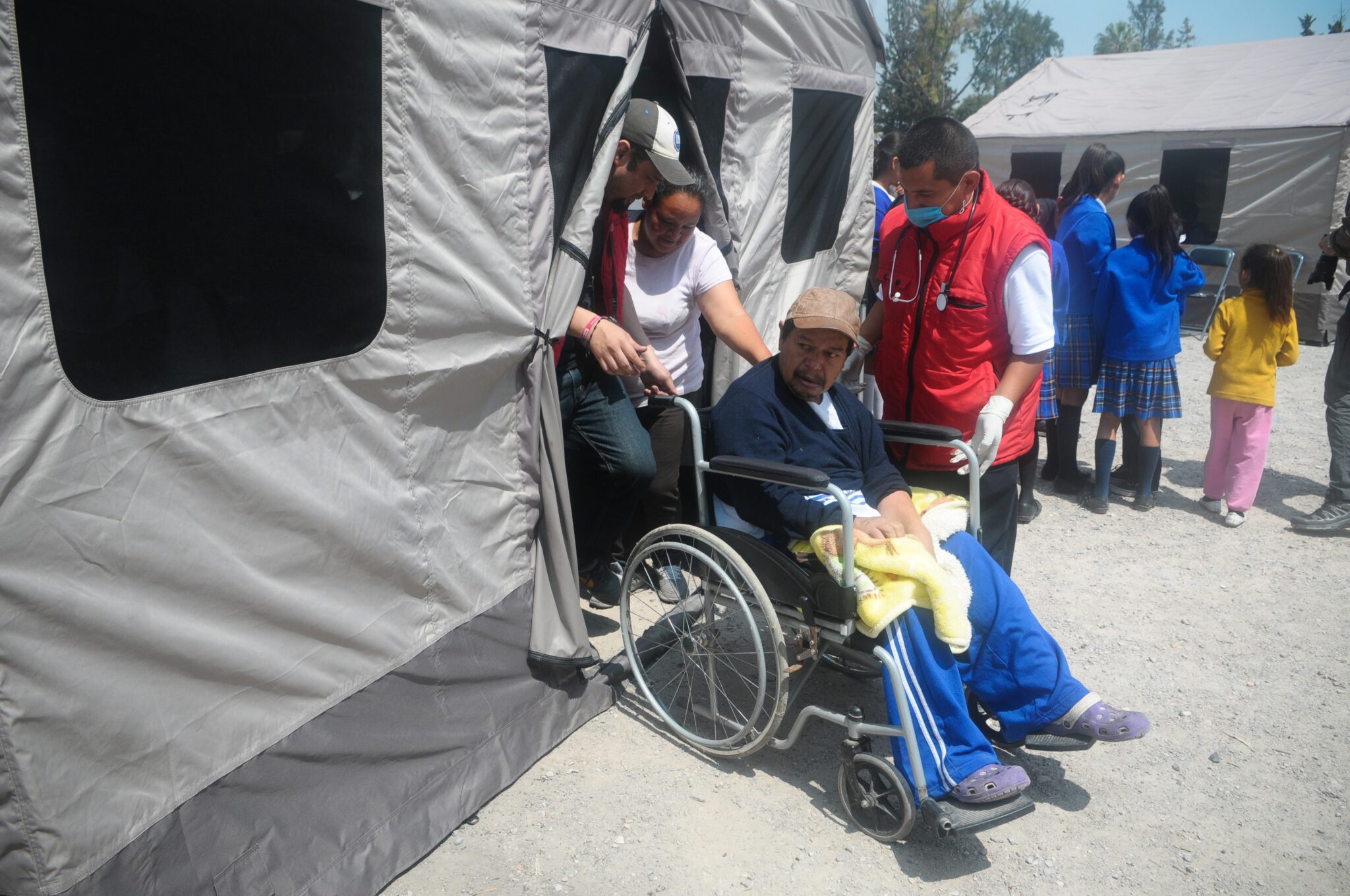 A man is helped into a mobile health clinic tent by family and staff. Photo by Direct Relief/Lara Cooper